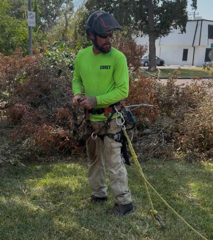 Corey Coupland, ISA Certified Arborist, on job site in lime green shirt with full climbing harness and rigging gear